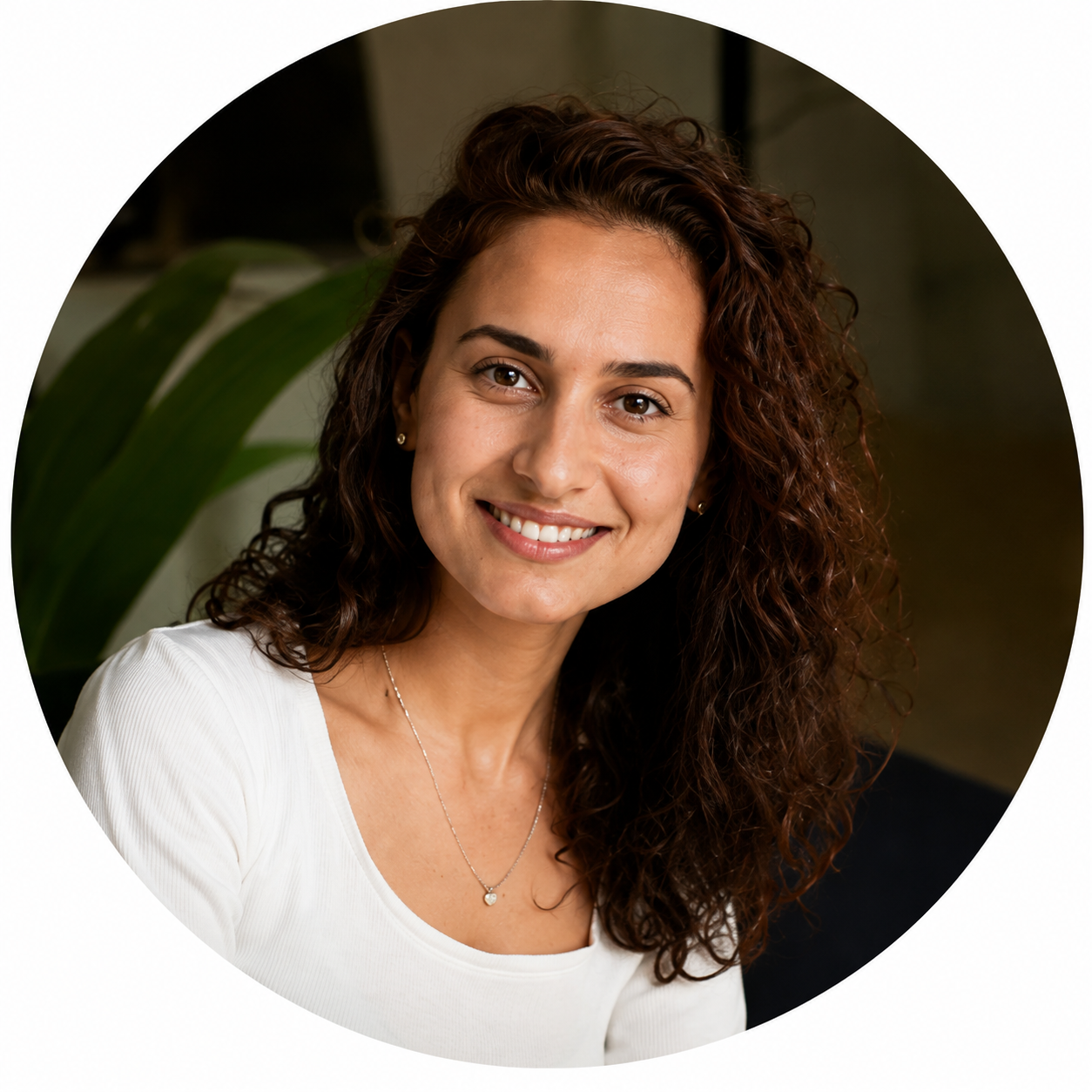 Portrait circulaire d'une femme souriante aux cheveux bouclés portant un top blanc et un pendentif délicat