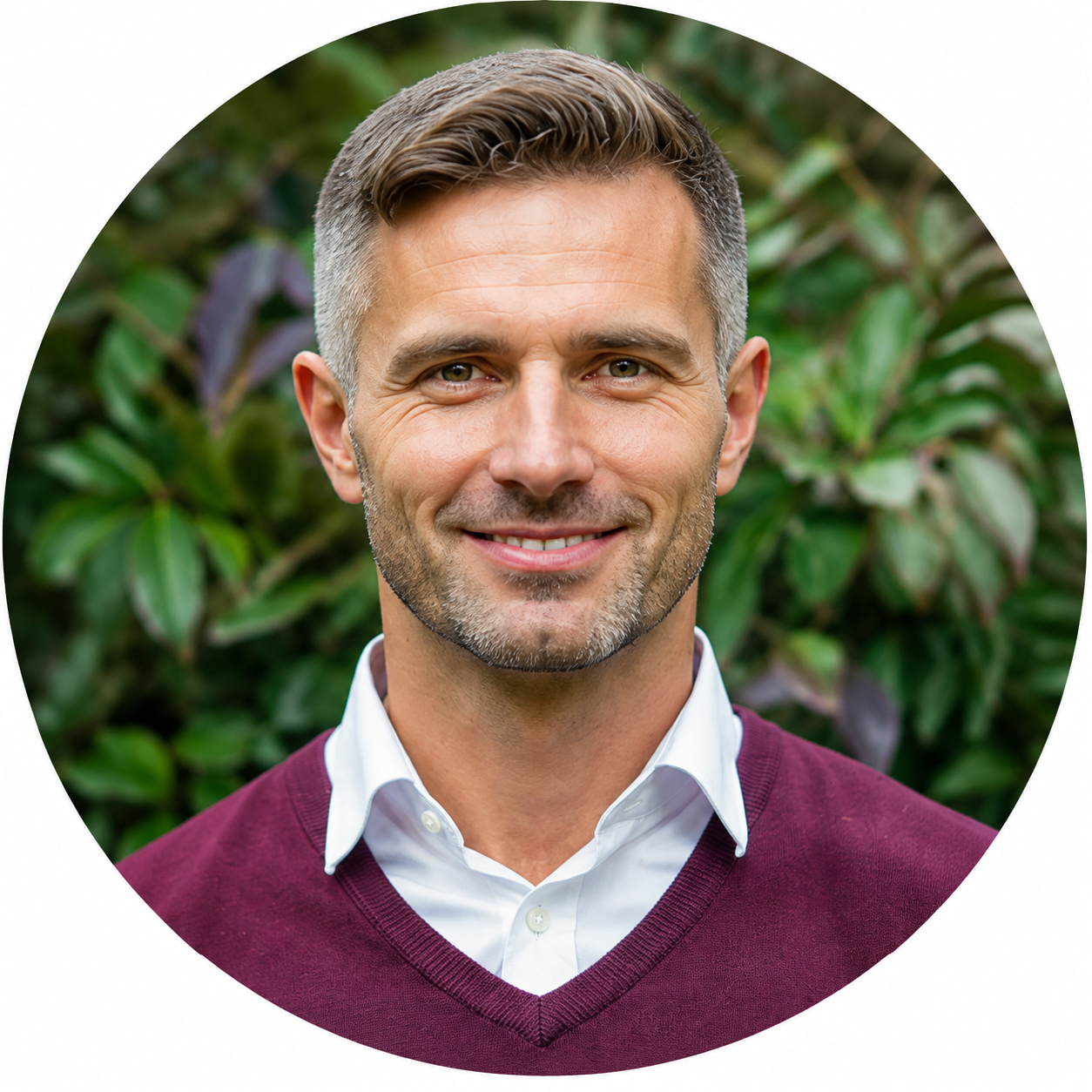 Portrait circulaire de Marc souriant portant un pull bordeaux et une chemise blanche, fond feuillage (contact)