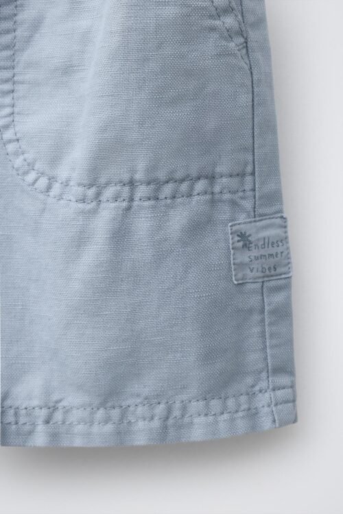 Short garçon en laine gris clair, détail poche et couture visible, étiquette côté