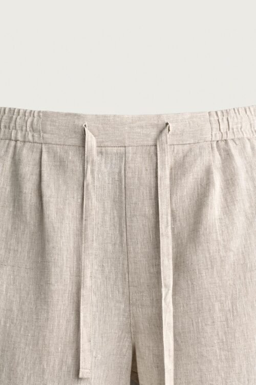 Short en lin naturel écru avec cordon ajustable à taille élastiquée, texture visible et plis devant